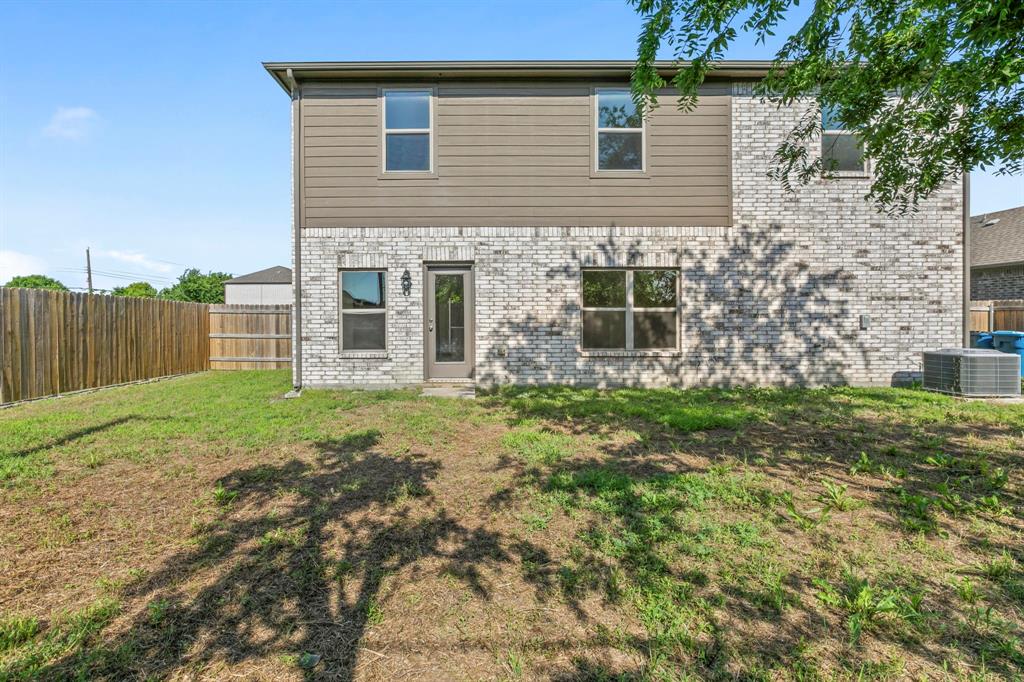 Rear exterior featuring a mix of light-toned brick and horizontal siding, multiple windows, a rear entry door with an exterior light fixture, and a wood privacy fence