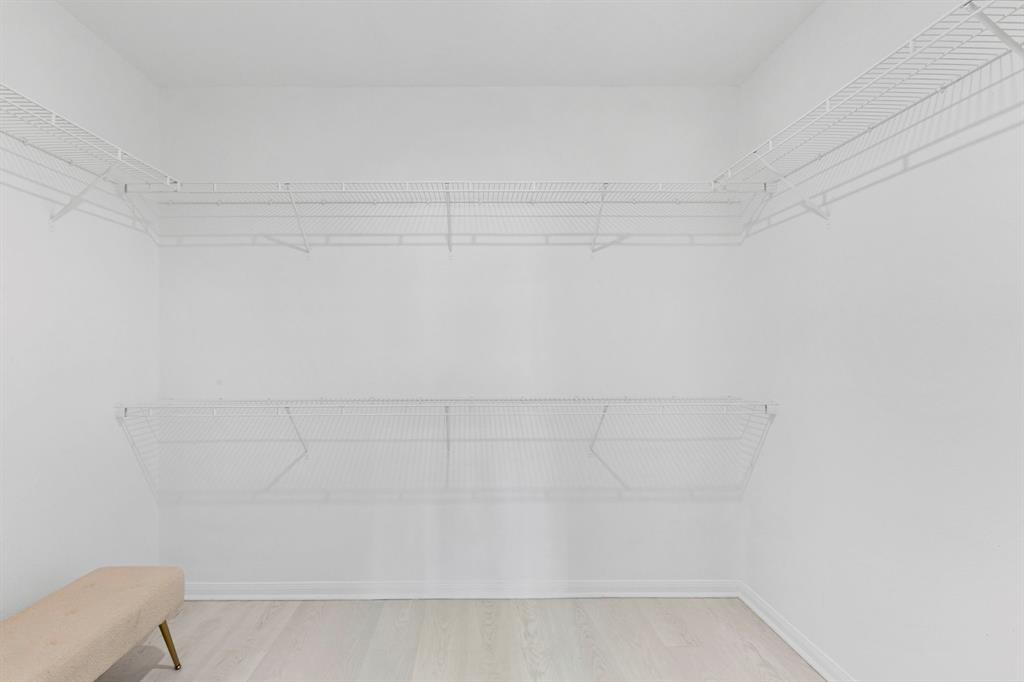 Spacious walk-in closet featuring white wire shelving, light wood-finish flooring, and white baseboards