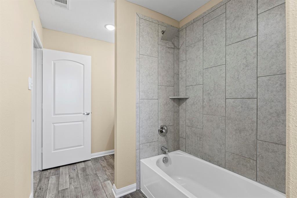 Bathroom featuring a white bathtub, chrome fixtures, and grey large-format tile surround