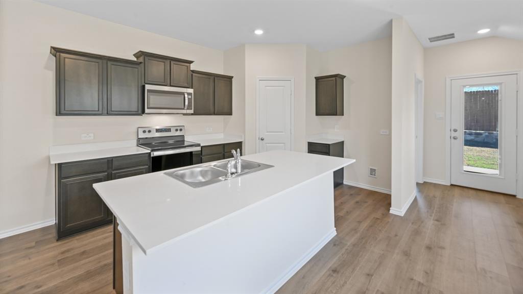 Kitchen featuring an expansive island with a double basin sink, dark wood cabinetry, white countertops, and stainless steel appliances including a range and microwave