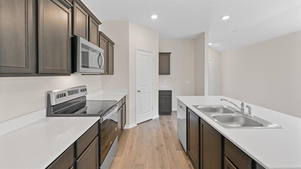 Modern kitchen featuring dark wood cabinetry, light countertops, stainless steel appliances including an electric range and microwave, and wood-finish flooring