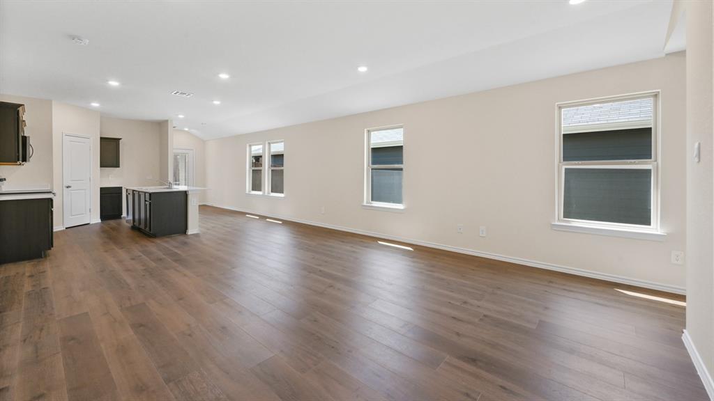 Open-concept living area featuring wood-finish flooring, recessed lighting, multiple windows, and a kitchen island with dark cabinetry