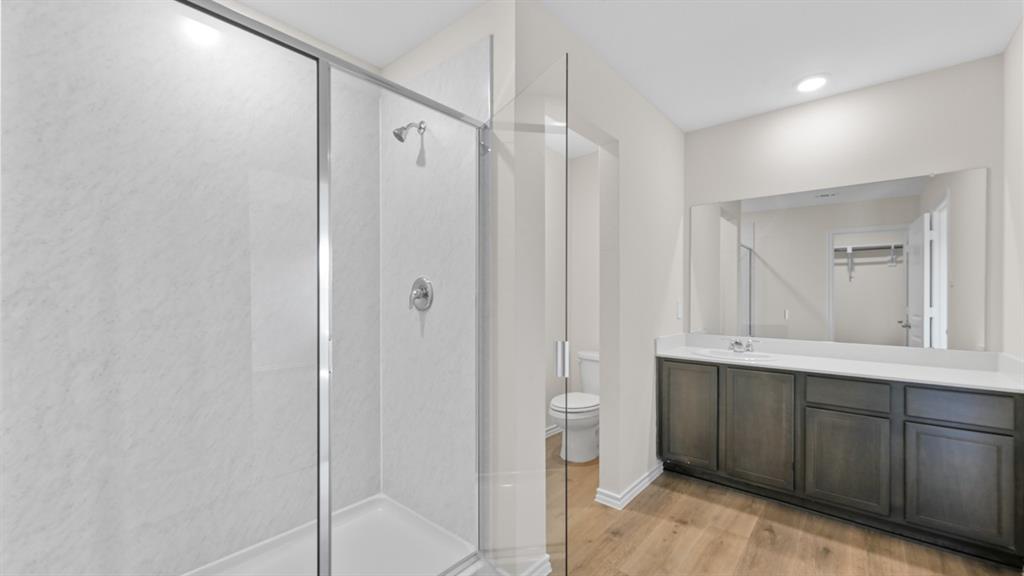 Bathroom featuring a glass-enclosed shower, wood-finish flooring, and a vanity with a white countertop and dark cabinetry