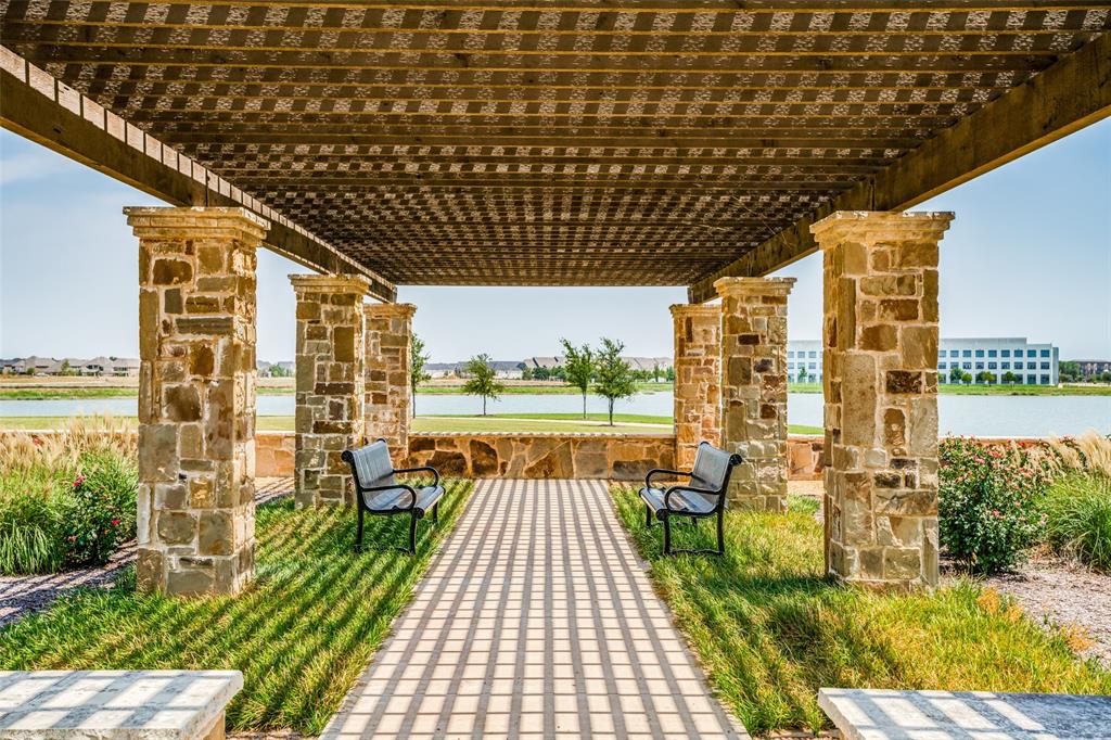 Stone-clad pergola structure with a slatted roof, featuring a paved pathway and flanking green spaces