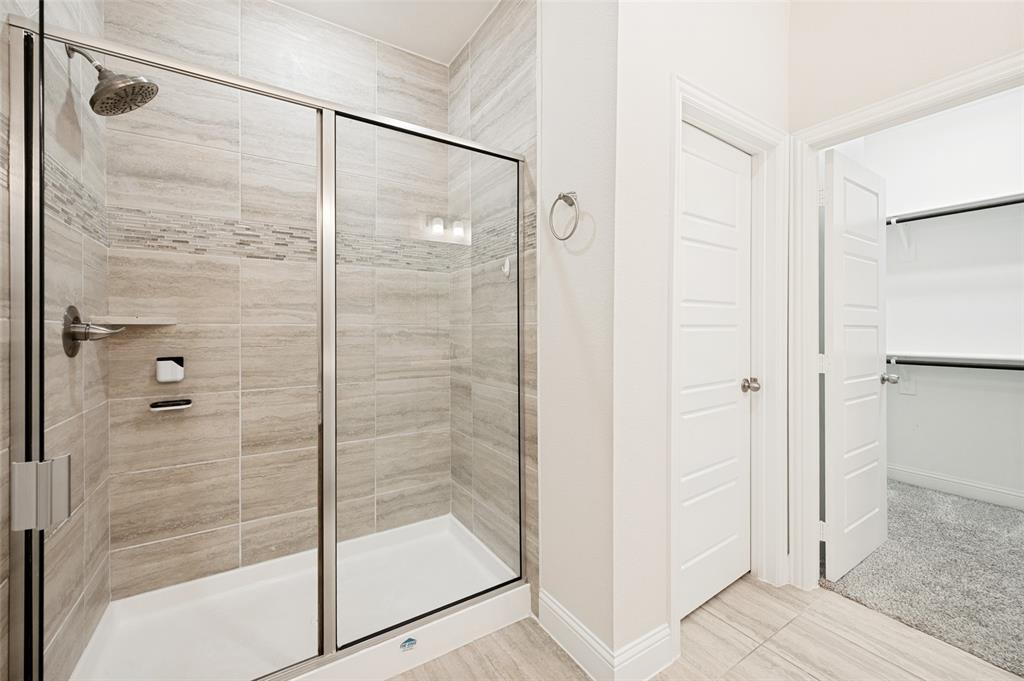 Shower enclosure with glass doors, a rainfall showerhead, and a tiled surround with decorative accents