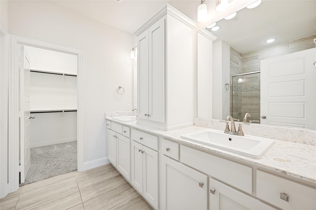 Bathroom featuring dual rectangular sinks set into stone-finish countertops, extensive white cabinetry, a large vanity mirror, and tile flooring