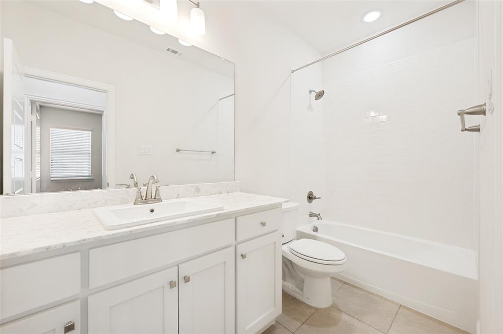 Bathroom featuring a white vanity with an undermount sink, a light-toned countertop, a large wall-mounted mirror, and a shower-over-tub combination with subway tile surround