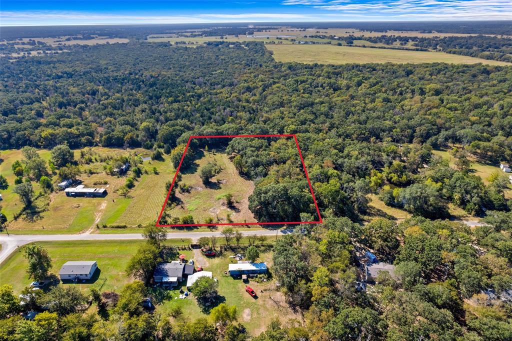 Expansive acreage featuring a mix of cleared areas and mature trees, bordered by a paved road Expansive acreage featuring a mix of cleared areas and mature trees, bordered by a paved road