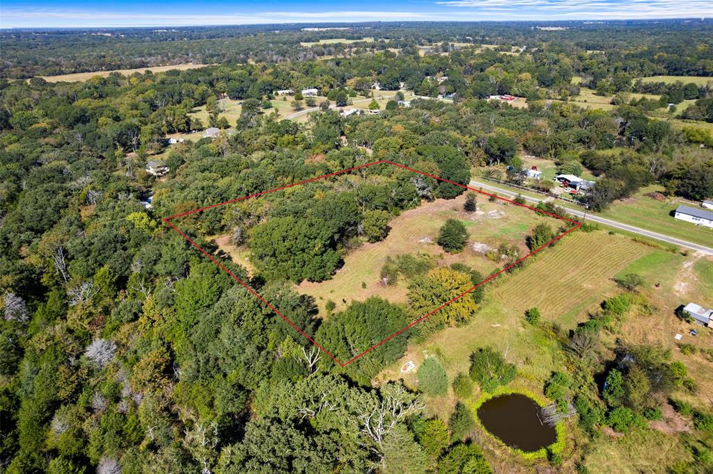 Expansive land parcel featuring a natural pond, a cultivated agricultural area, and a mix of mature trees and open clearings