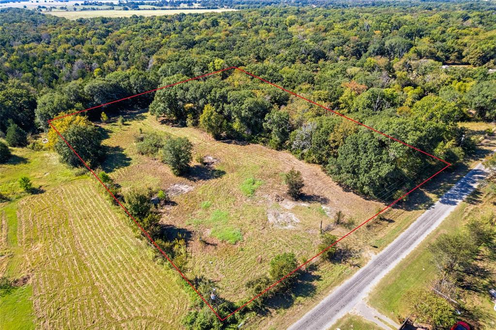 Expansive undeveloped land featuring a mix of open areas and mature trees, bordered by a paved road