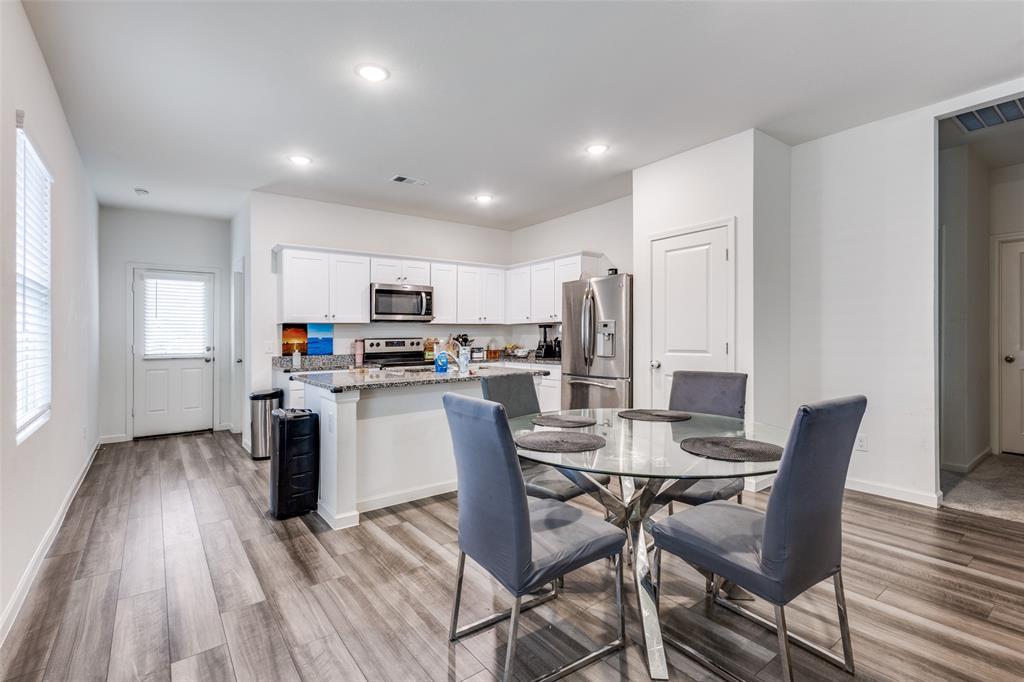 Open-concept kitchen and dining area featuring wood-finish flooring, white cabinetry, granite-style countertops, stainless steel appliances, and recessed lighting