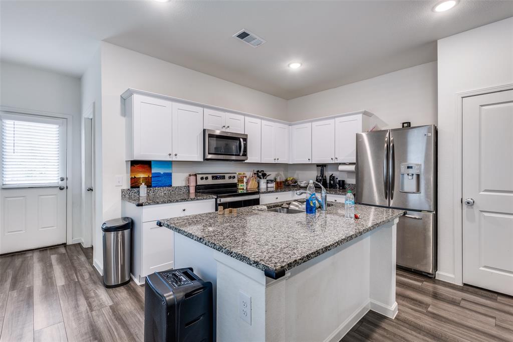 Kitchen featuring white cabinetry, granite countertops, stainless steel appliances, a center island with a sink, and wood-finish flooring
