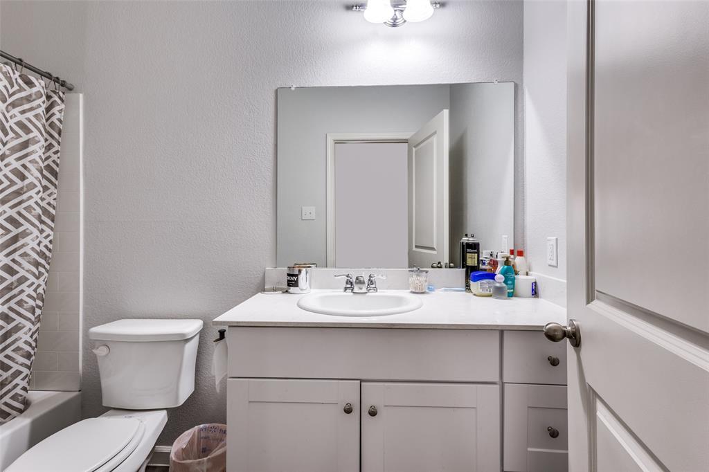 Bathroom featuring a white vanity with integrated sink, a large wall-mounted mirror, brushed nickel hardware, and a tub with tiled surround