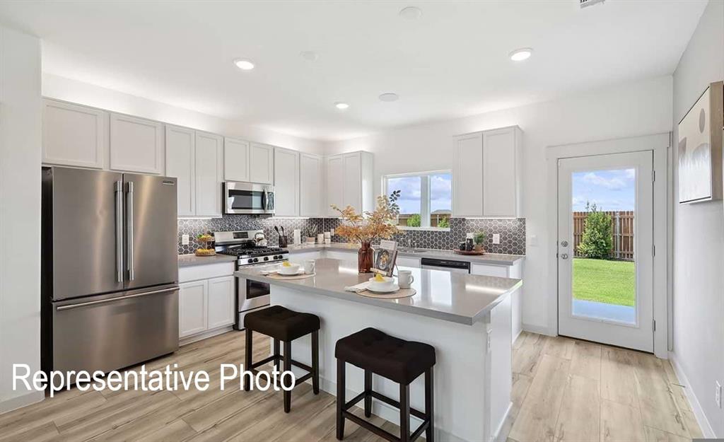Modern kitchen featuring light wood-finish flooring, white cabinetry, stainless steel appliances, and a hexagon tile backsplash