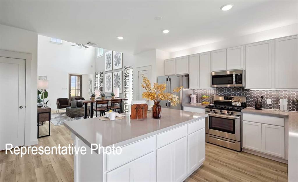 Open-concept kitchen featuring an expansive island with countertop seating, white shaker cabinetry, stainless steel appliances, and a hexagon tile backsplash