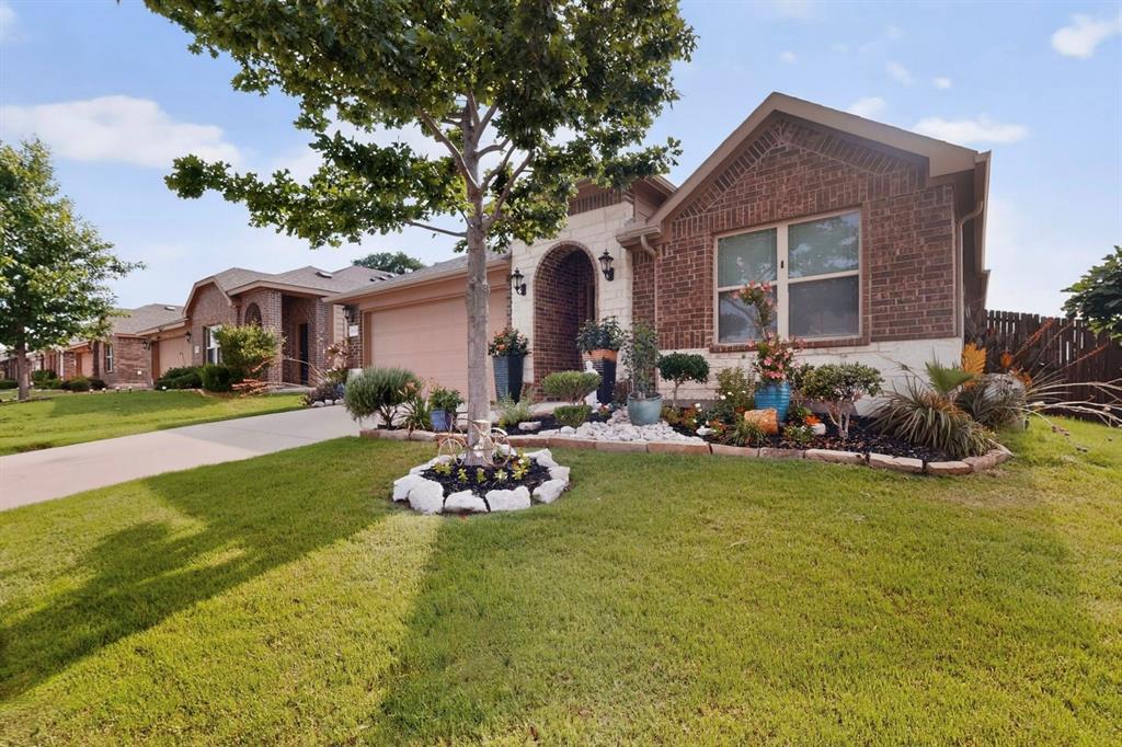 Brick and stone facade residence featuring an arched entryway, established landscaping, two-car garage, and a fenced backyard
