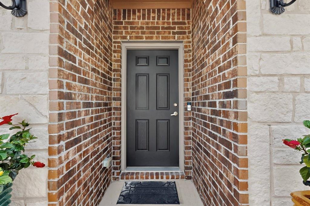 Inviting entry featuring a paneled black door, complementary light stone and brick facade, and an integrated smart doorbell system