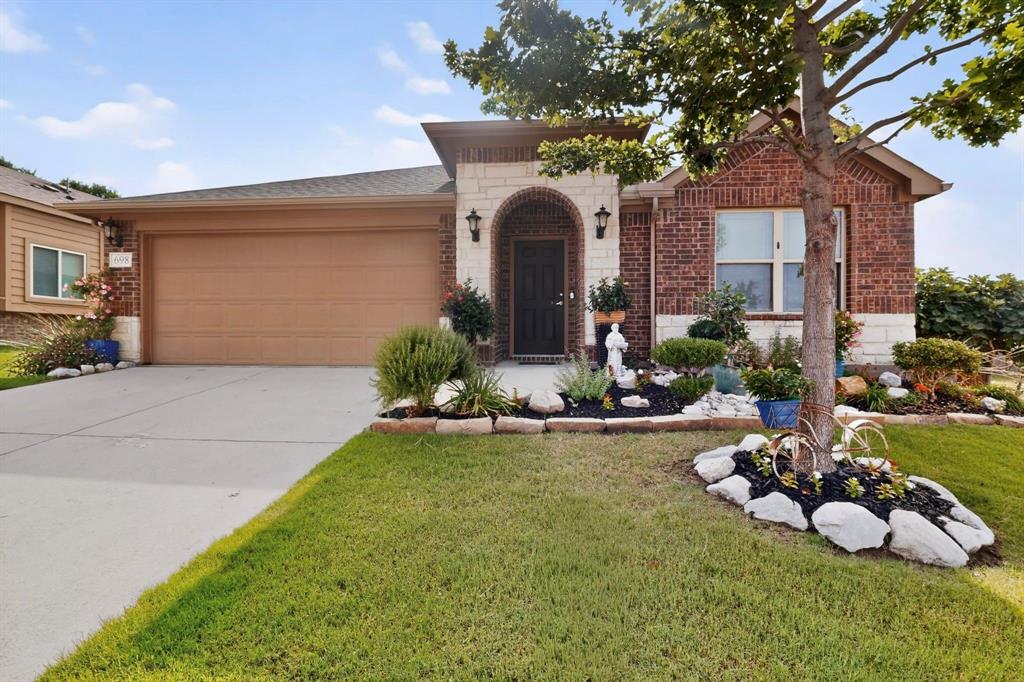 Brick and stone façade residence featuring an arched entry, a two-car garage, and established landscaping