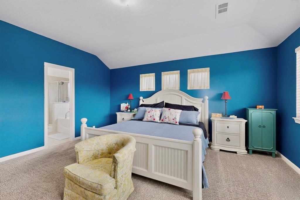 Carpeted bedroom featuring a vaulted ceiling, multiple windows with white blinds, and an entryway to a full bathroom with a shower and tub combination