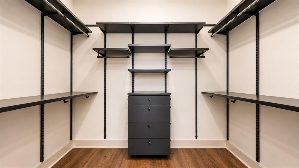 Custom closet system featuring dark wood-finish flooring, white walls, and a central five-drawer dresser