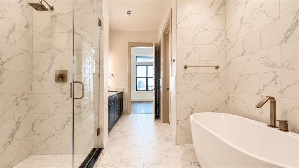 Spacious bathroom featuring marble-look tile flooring and walls, a freestanding soaking tub with bronze-finish fixtures, and a frameless glass shower enclosure with a rain showerhead