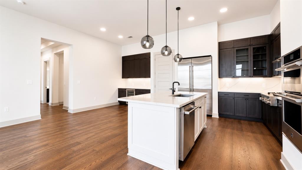 Gourmet kitchen featuring a central island with a white countertop and seating, dark wood-finish cabinetry, stainless steel appliances, and wood-finish flooring