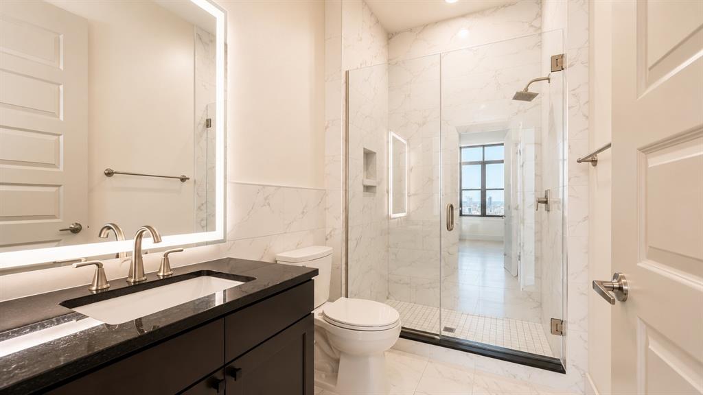 Contemporary bathroom featuring a dark wood vanity with a black countertop and an integrated sink, illuminated by a backlit mirror