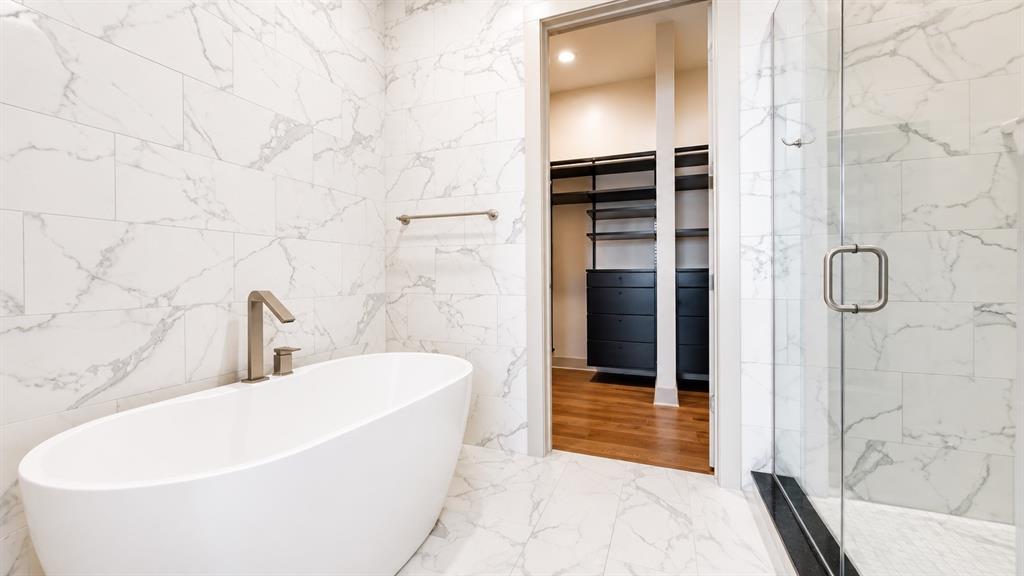 Freestanding soaking tub with brushed nickel fixtures set against marble-look tile walls
