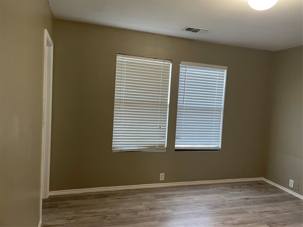 Interior space featuring wood-finish flooring, two windows with blinds, a white ceiling light fixture, and neutral painted walls