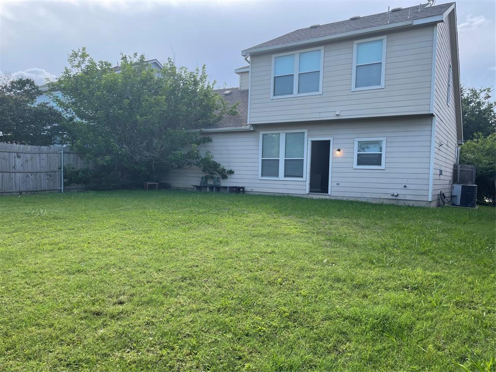 Expansive rear lawn featuring a privacy fence, established trees, and a two-story exterior with multiple windows