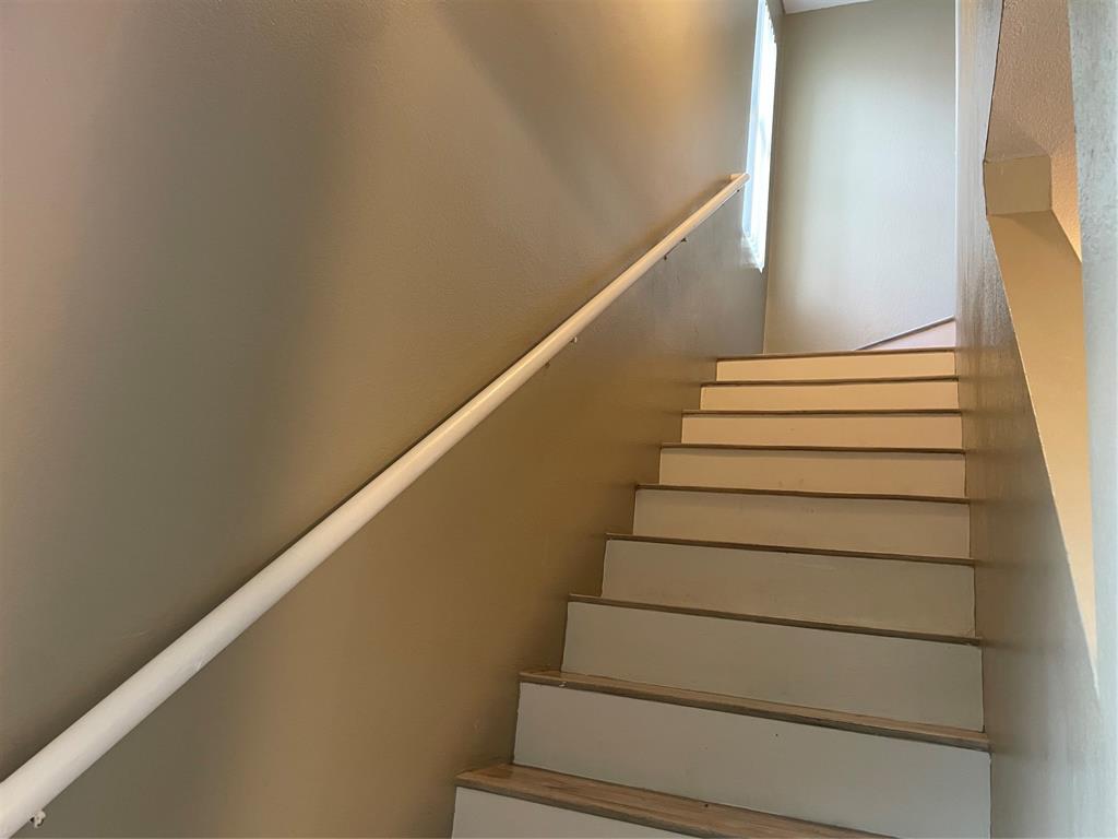 Staircase featuring wood-finish treads and risers, a white handrail, and light tan wall paint