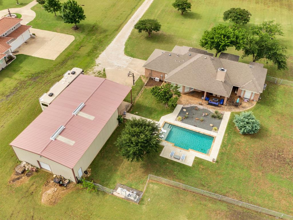 Expansive property featuring a rectangular swimming pool with concrete decking, a covered patio, a detached metal-sided outbuilding with a metal roof, and a gravel driveway