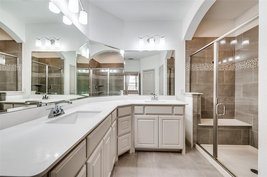 Bathroom with double vanity, large mirror, and stall shower, offering a spacious primary or secondary bath setup with extra counter space and storage, appealing to buyers who want a McKinney Texas townhouse with updated bathrooms, double sinks, and convenient layout in a well located Collin County community