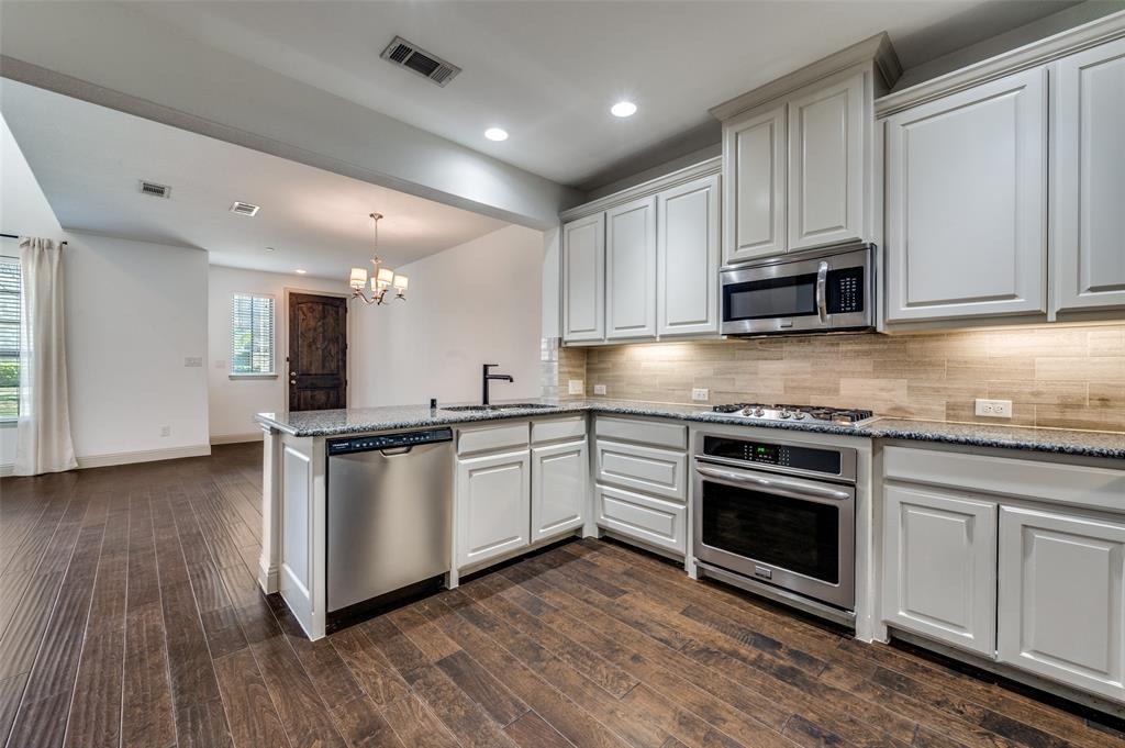 Kitchen with peninsula, light stone counters, stainless steel appliances, chandelier, and open sightlines to the living and dining spaces, creating a functional open kitchen layout that is perfect for casual dining, bar seating, entertaining guests, and everyday family life in this McKinney Texas townhome in North Texas. Kitchen with peninsula, light stone counters, stainless steel appliances, chandelier, and open sightlines to the living and dining spaces, creating a functional open kitchen layout that is perfect for casual dining, bar seating, entertaining guests, and everyday family life in this McKinney Texas townhome in North Texas.