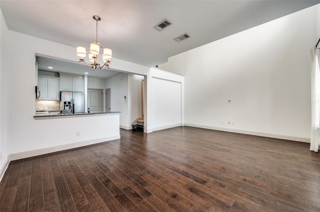 Large unfurnished living room with hanging lights, dark wood finished floors, and multiple windows bringing in natural light, showcasing flexible furniture layout options and open sightlines into adjacent spaces, ideal for homeowners who want a McKinney Texas townhouse with a big room for gatherings, entertaining, and daily living near major DFW employment centers. Large unfurnished living room with hanging lights, dark wood finished floors, and multiple windows bringing in natural light, showcasing flexible furniture layout options and open sightlines into adjacent spaces, ideal for homeowners who want a McKinney Texas townhouse with a big room for gatherings, entertaining, and daily living near major DFW employment centers.