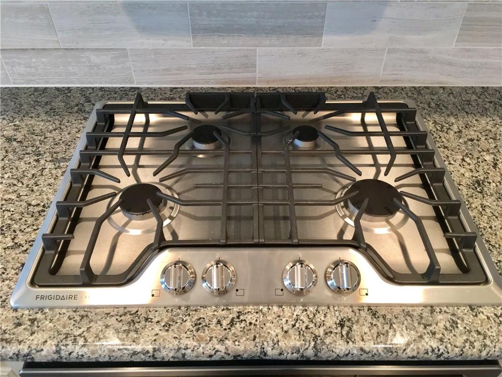 Close up of kitchen showing stainless steel gas cooktop, oven, detailed tile backsplash, stone counters, and modern controls, appealing to buyers searching for a McKinney Texas townhouse with stainless steel appliances, gas cooking, and stylish kitchen design in a convenient Collin County location near major roads and retail.