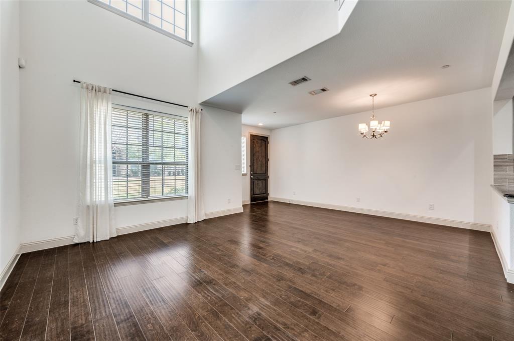 Unfurnished living room in this McKinney TX townhome for sale featuring suspended lighting, soaring high ceiling, dark wood finished floors, neutral wall color, and open concept design, perfect for buyers searching for a modern traditional McKinney townhome with spacious living area, natural light, and room for entertaining in Collin County. Unfurnished living room in this McKinney TX townhome for sale featuring suspended lighting, soaring high ceiling, dark wood finished floors, neutral wall color, and open concept design, perfect for buyers searching for a modern traditional McKinney townhome with spacious living area, natural light, and room for entertaining in Collin County.