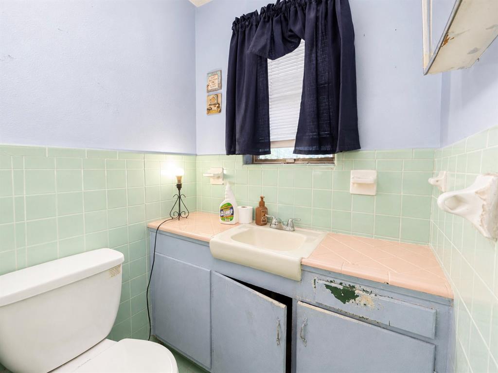 Bathroom featuring light blue wall paint, green square wall tiles, a built-in vanity with a pink countertop and integrated sink, and a white toilet