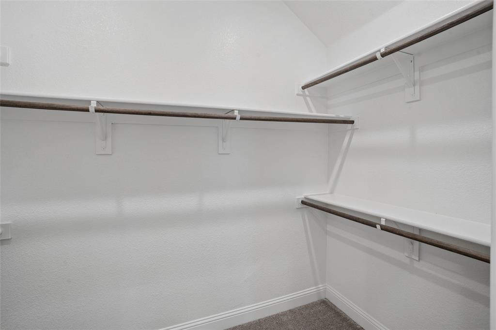 White-painted closet interior featuring multiple wooden hanging rods, white shelving, and white baseboards