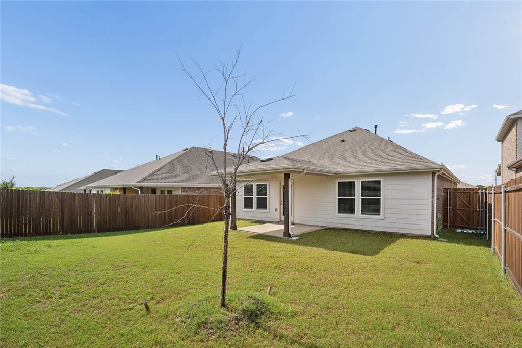 Expansive backyard featuring a green lawn, wood privacy fencing, and a covered patio with a concrete slab