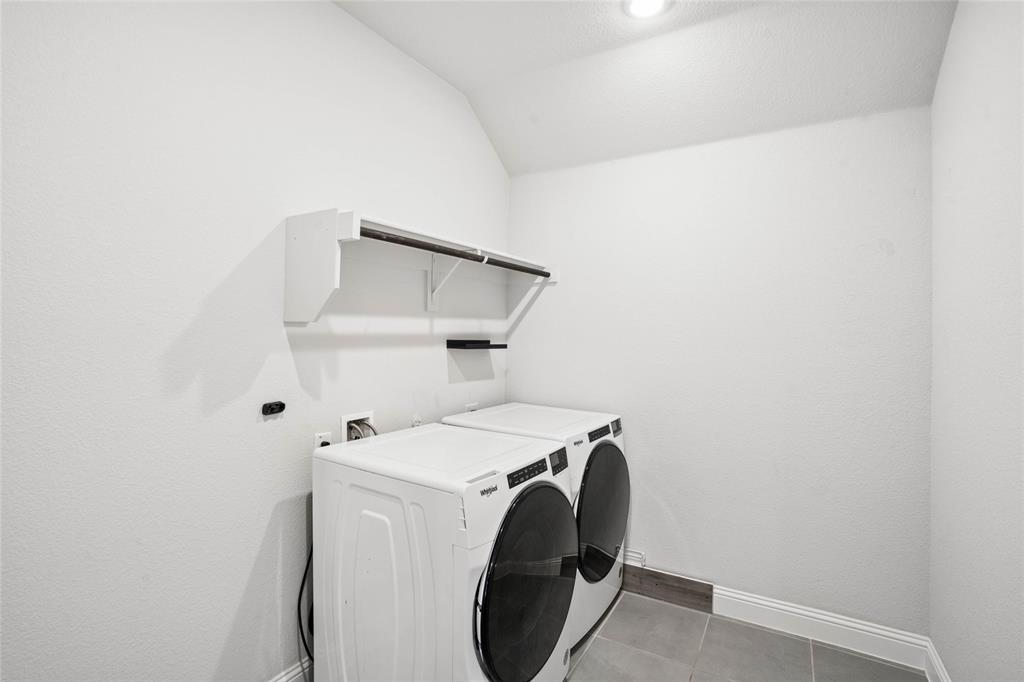 Dedicated laundry space featuring white textured walls, recessed ceiling lighting, a built-in shelf with a hanging rod, and grey tile flooring