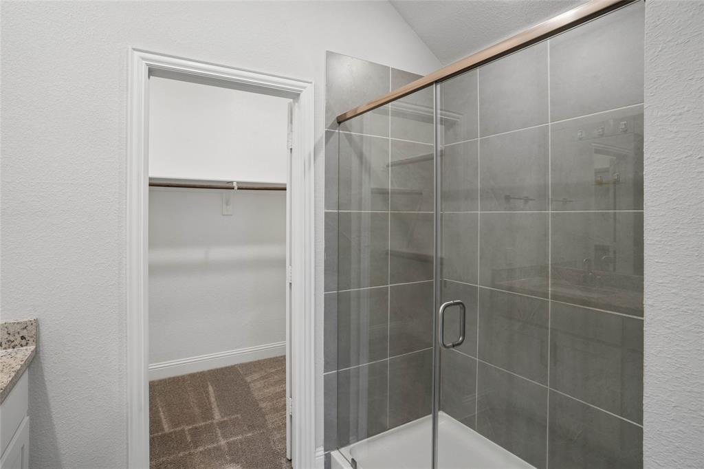 Glass-enclosed shower with gray square tile surround and bronze-finish framing