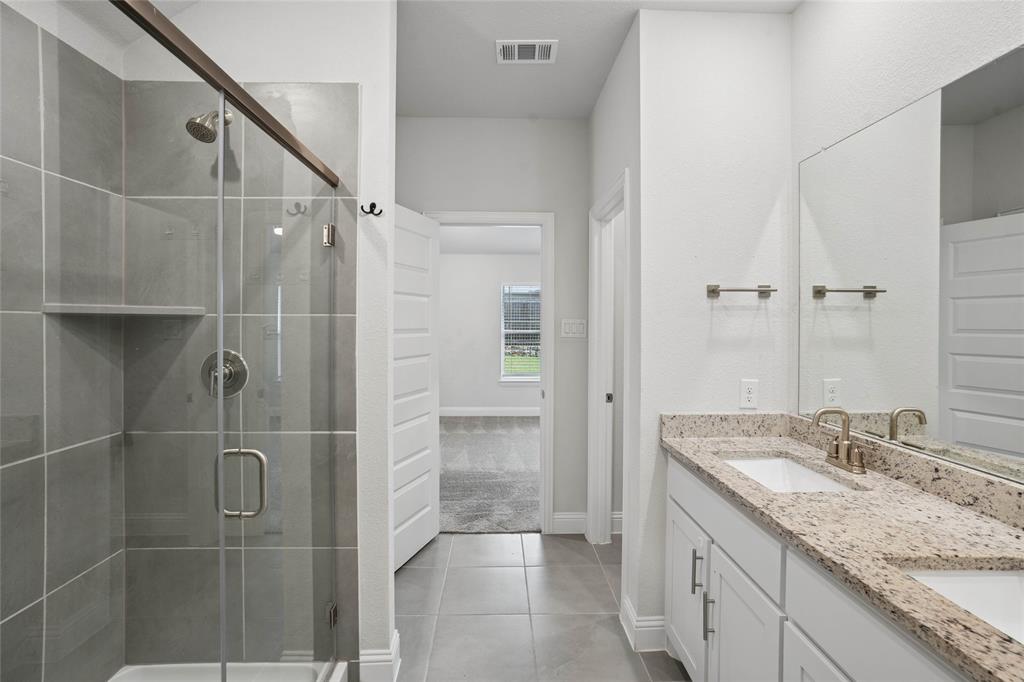 Bathroom featuring a glass-enclosed shower with tile surround, a dual vanity with light-toned countertops, and light-colored flooring