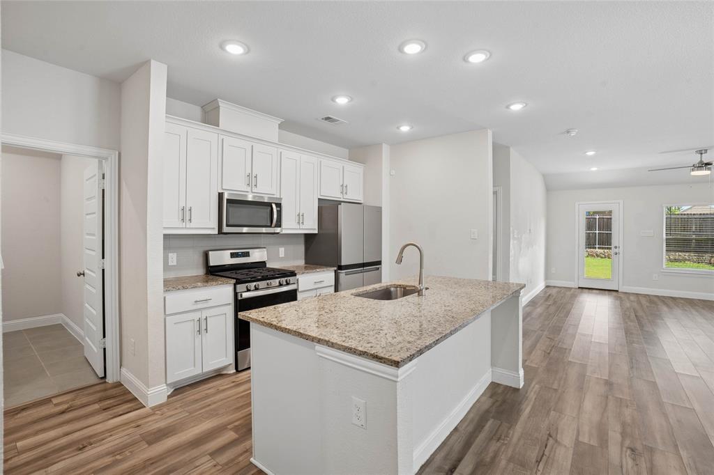 Modern kitchen featuring an island with an undermount sink, granite countertops, white cabinetry, stainless steel appliances, and wood-finish flooring Modern kitchen featuring an island with an undermount sink, granite countertops, white cabinetry, stainless steel appliances, and wood-finish flooring