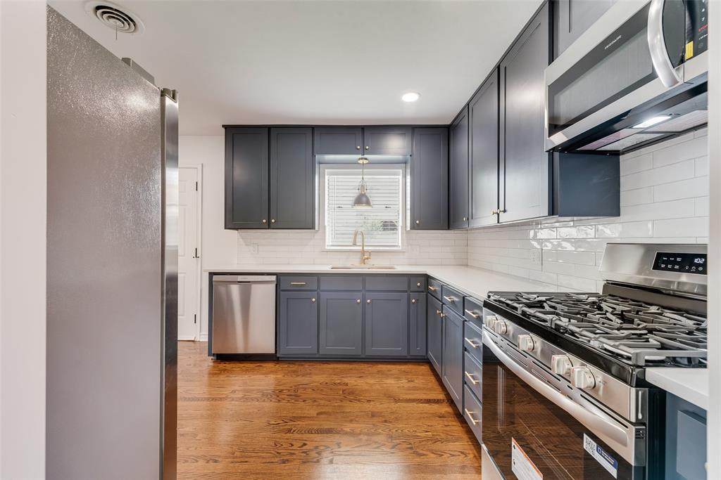 Contemporary kitchen featuring dark cabinetry, stainless steel appliances, a subway tile backsplash, light countertops, and wood-finish flooring