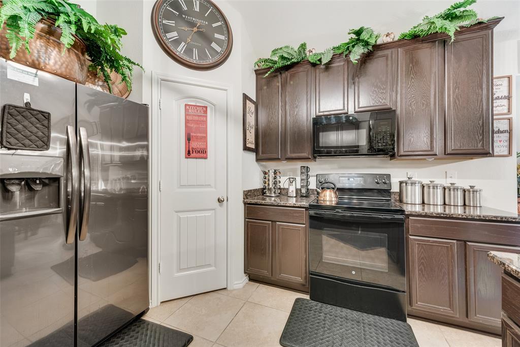 Kitchen featuring wood-finish cabinetry, stone countertops, stainless steel refrigerator, black electric range, and tile flooring