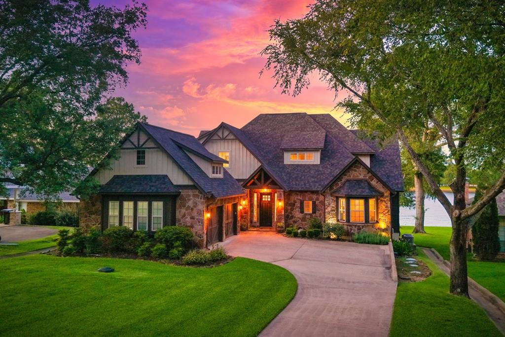 Hill Country style meets classic lakehouse charm in this waterfront home with a stone and wood exterior. Street side view showing the two car garage.