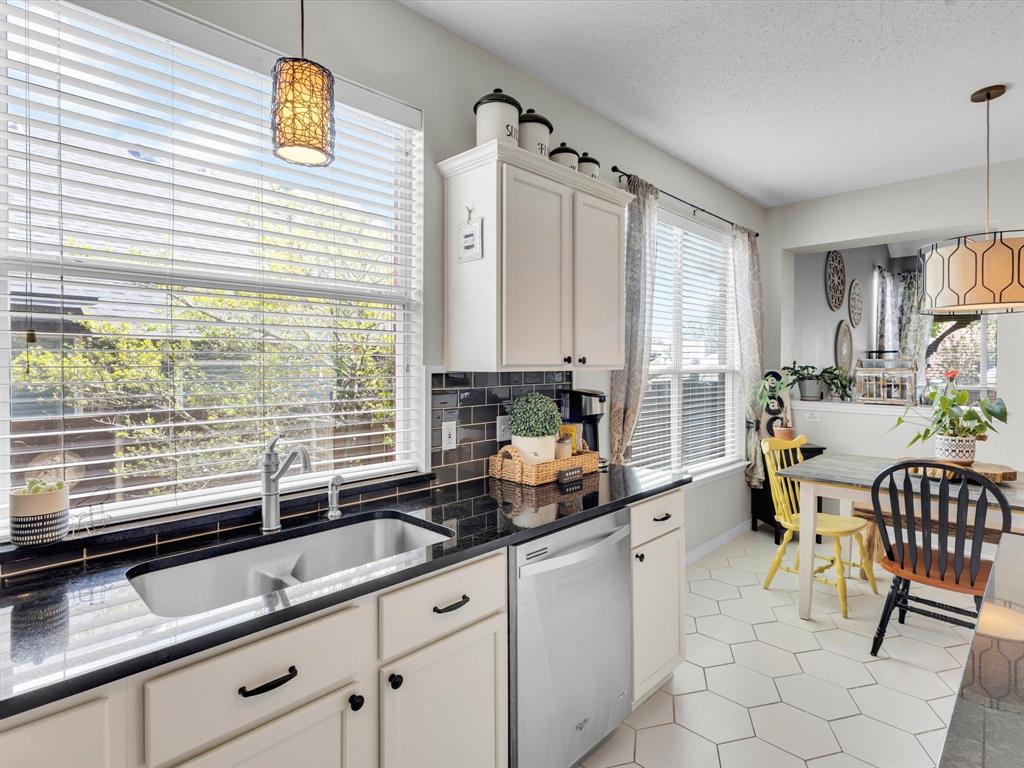 Kitchen featuring white cabinetry, black countertops, a subway tile backsplash, and a large window above the sink