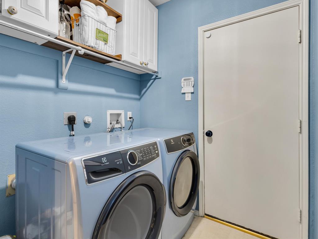 Dedicated laundry area featuring a light blue wall finish, white cabinetry, and a wood-finish shelf