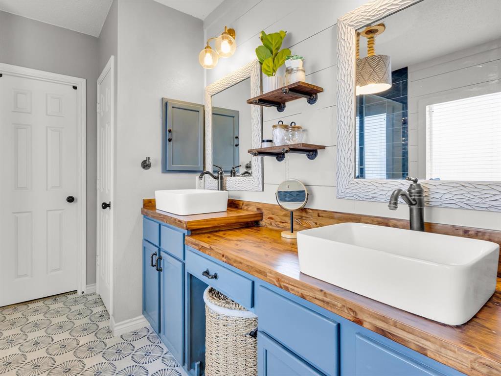 Dual vessel sinks set on a wood-finish countertop with blue cabinetry